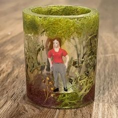 a glass cup with a photo of a woman in the woods on it sitting on a wooden table