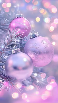 two pink christmas ornaments hanging from a pine tree with blurry lights in the background