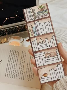 a person holding an open book in front of a laptop on a table with bookshelves