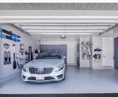 a car is parked in a garage with surfboards on the wall and snowboards hanging from the ceiling