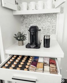 a coffee maker and some muffins are in the open drawer on this white shelf