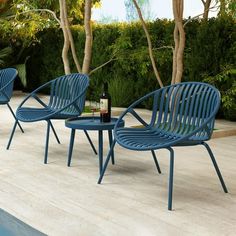 three blue chairs sitting next to a pool with a bottle of wine on the table