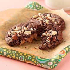 two chocolate cookies with nuts and milk on a napkin next to a glass of milk