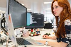 a woman sitting at a desk in front of two computer monitors