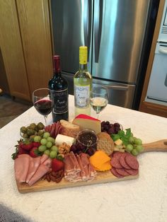 a wooden cutting board topped with cheese, meat and fruit next to a bottle of wine