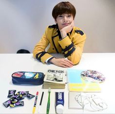 a young man sitting at a table with his hand on his chin, surrounded by school supplies