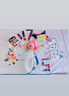 a baby laying on top of a white blanket covered in lots of toys and items