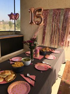 a table set up for a birthday party with pink plates and confetti on it