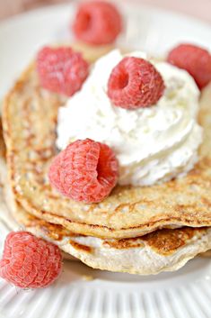 pancakes with whipped cream and raspberries on a white plate