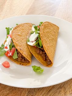 two tacos with lettuce and tomatoes on a white plate sitting on a wooden table