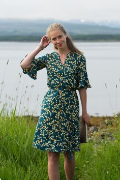 a woman in a green dress is standing by the water with her hand on her head