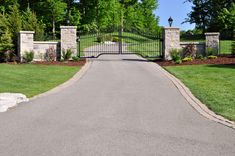 a driveway leading to a gated entrance into a lush green park