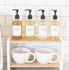 three soap dispensers are sitting on a shelf next to coffee mugs