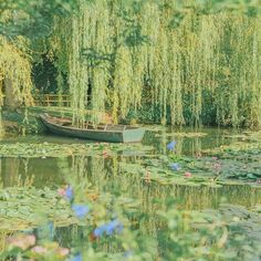 a small boat floating on top of a lake surrounded by lily pads and willow trees