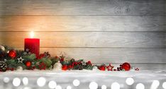 a lit candle surrounded by christmas decorations on a wooden background with lights and snowflakes