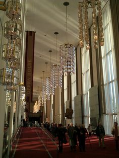 people are walking through the lobby of a building with chandeliers hanging from the ceiling