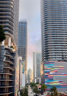 some very tall buildings in the city with colorful lines on their sides and trees around them