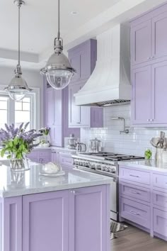 a kitchen with purple cabinets and white counter tops, an island in the middle has flowers on it