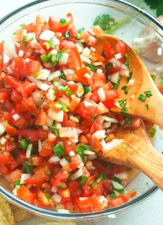 a wooden spoon filled with chopped up tomatoes and onions in a glass bowl next to tortilla chips