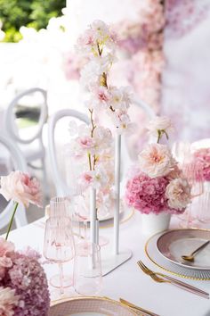 the table is set with pink and white flowers in tall vases on each side