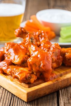 a wooden plate topped with meat covered in marinara sauce and carrots next to a glass of beer