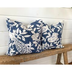 two blue and white pillows sitting on top of a wooden bench next to a plant