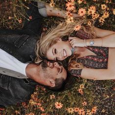 a man and woman laying on the ground next to each other with flowers in the background