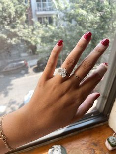 a woman's hand with red nails and a ring on her finger, next to a window