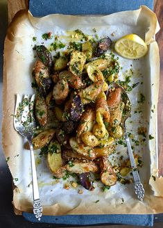 a plate with shrimp, potatoes and lemon on it next to a knife and fork