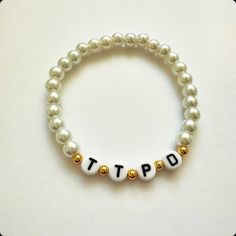 a white beaded bracelet with gold beads and the wordtip written in small letters