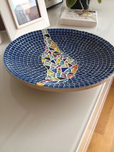 a blue mosaic bowl sitting on top of a counter next to a framed photo and potted plant