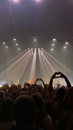 a large crowd at a concert with their hands up in the air and lights on