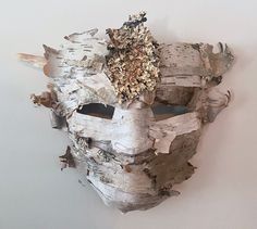 a mask made out of wood is hanging on the wall next to a white wall