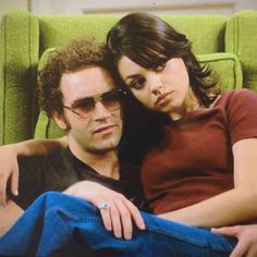 a man sitting next to a woman on top of a green chair with her arm around him