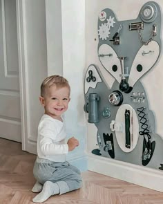 a little boy sitting on the floor in front of a wall with clocks and magnets