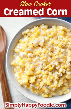 a white bowl filled with creamed corn on top of a blue cloth next to a wooden spoon