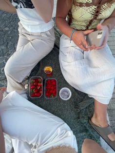 two women sitting on the ground with strawberries in plastic containers next to each other