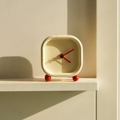 a small white clock sitting on top of a shelf next to a wall with a shadow