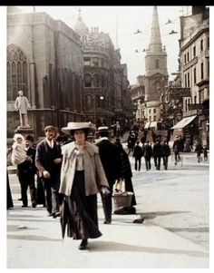 an old photo of people walking down the street with buildings in the backgroud