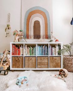 a white bookcase filled with lots of books next to a wall mounted rainbow painting