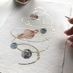 a person is drawing on paper with gold chains and space images in the background,