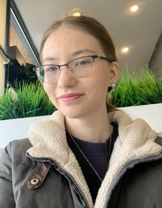 a woman wearing glasses is posing for the camera in front of a planter with green grass