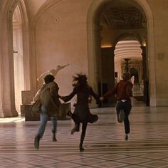 three people are running in the middle of a building with arches and columns on either side of them