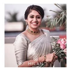 a woman in a white sari holding flowers and smiling at the camera with her hands on her hips