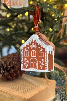 a gingerbread house ornament hanging from a christmas tree with an open book