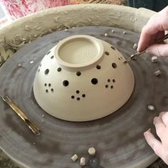 two hands are working on a pottery bowl with holes in the middle and small stones around it