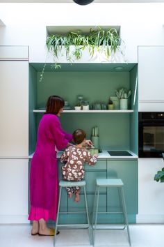 a woman standing next to a child sitting at a table in front of a shelf filled with potted plants