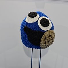 a blue crocheted hat with two eyes and a brown ball on it's head