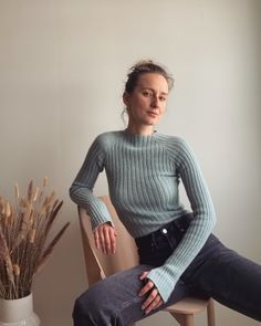 a woman sitting in a chair next to a potted plant and looking at the camera