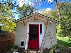 a small shed with a red door and ladder to the side, next to a tree